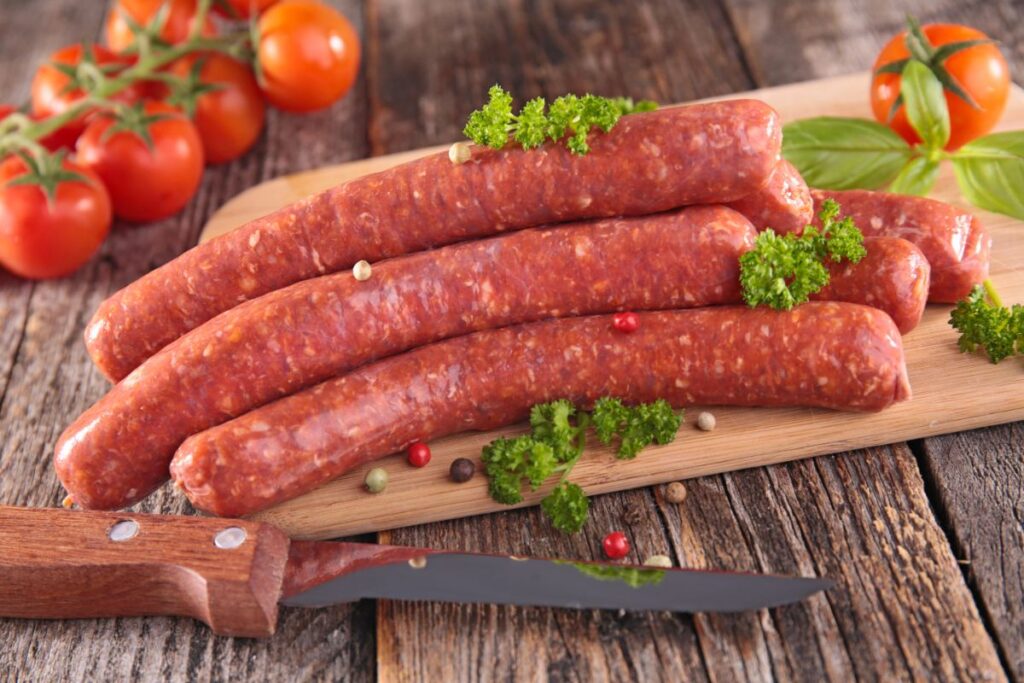 Des merguez et des tomates sur une plachette avec un couteau de côté