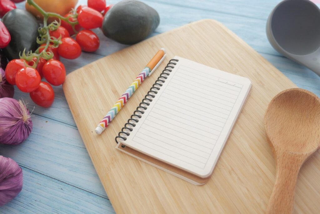 Un carnet sur une planchette en bois avec une cuillère et des légumes