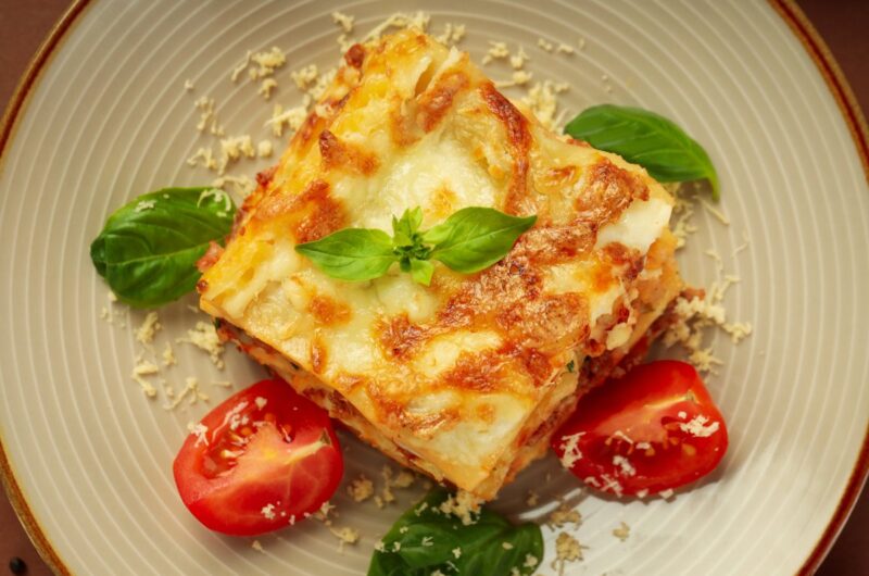 Une assiette de lasagne avec des tomates et des feuilles vertes