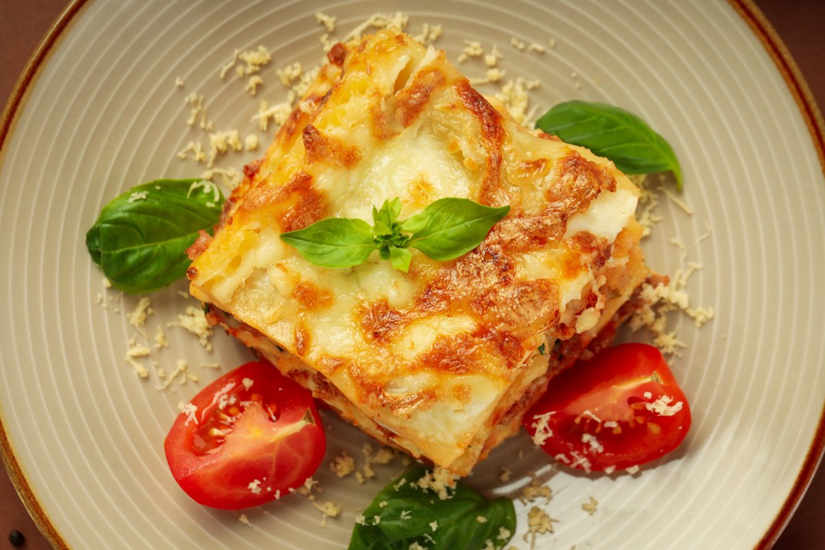 Une assiette de lasagne avec des tomates et des feuilles vertes