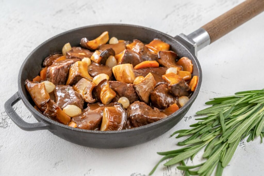 Du boeuf bourguignon avec des champignons et des oignons dans la poêle