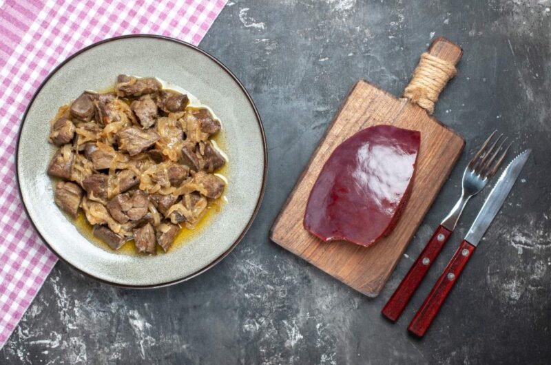 Un plat de foie de veau cuit et un foie de veau sur une planchette en bois