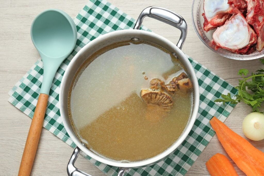 Un bol rempli de fond de veau avec une louche et des carottes sur la table