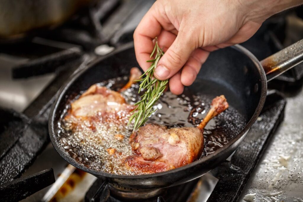 Une personne qui ajoute du romarin dans le confit du canard