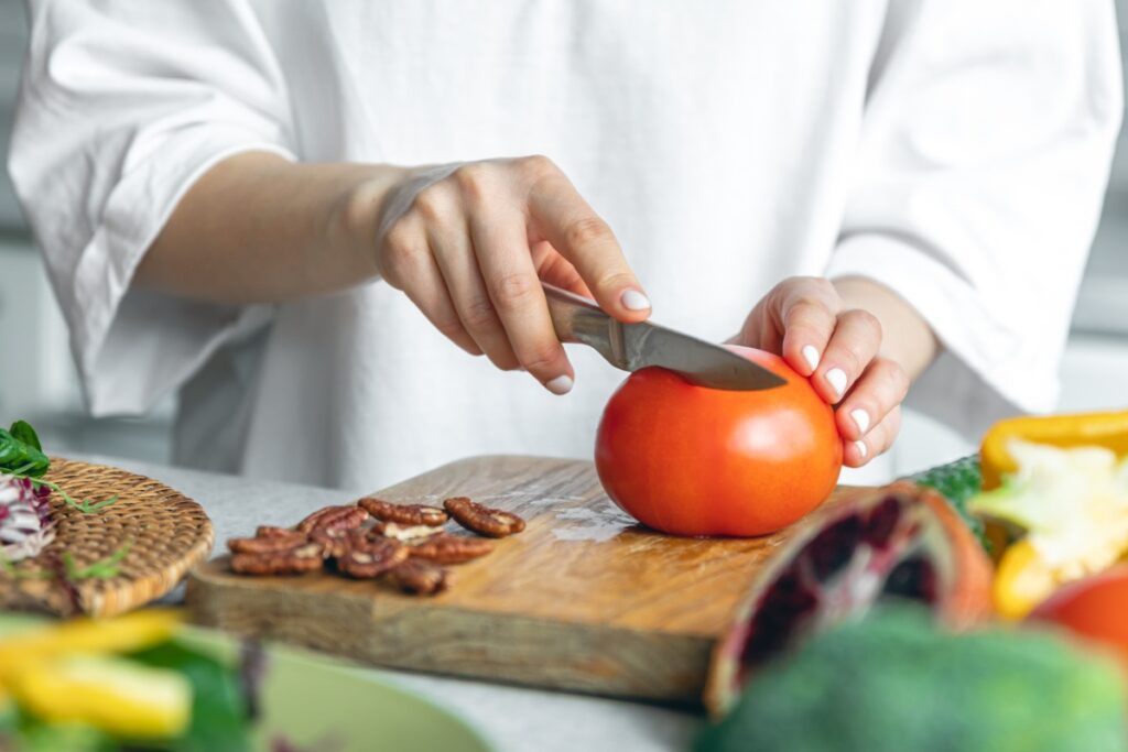 Une femme qui coupe une tomate sur une planchette en bois