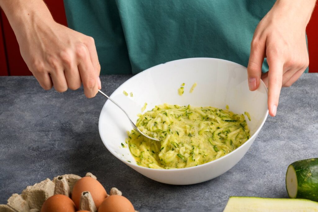 Une personne mélangeant des courgettes et des oeufs dans un bol