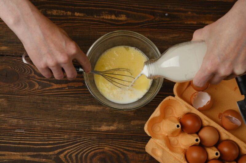 Une personne qui verse du lait dans un bol avec des oeufs