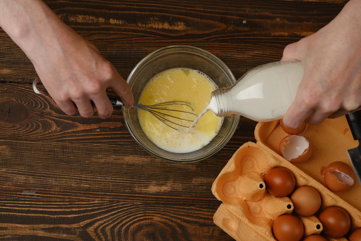 Une personne qui verse du lait dans un bol avec des oeufs